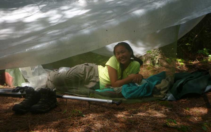A young person smiles from under a tarp shelter.